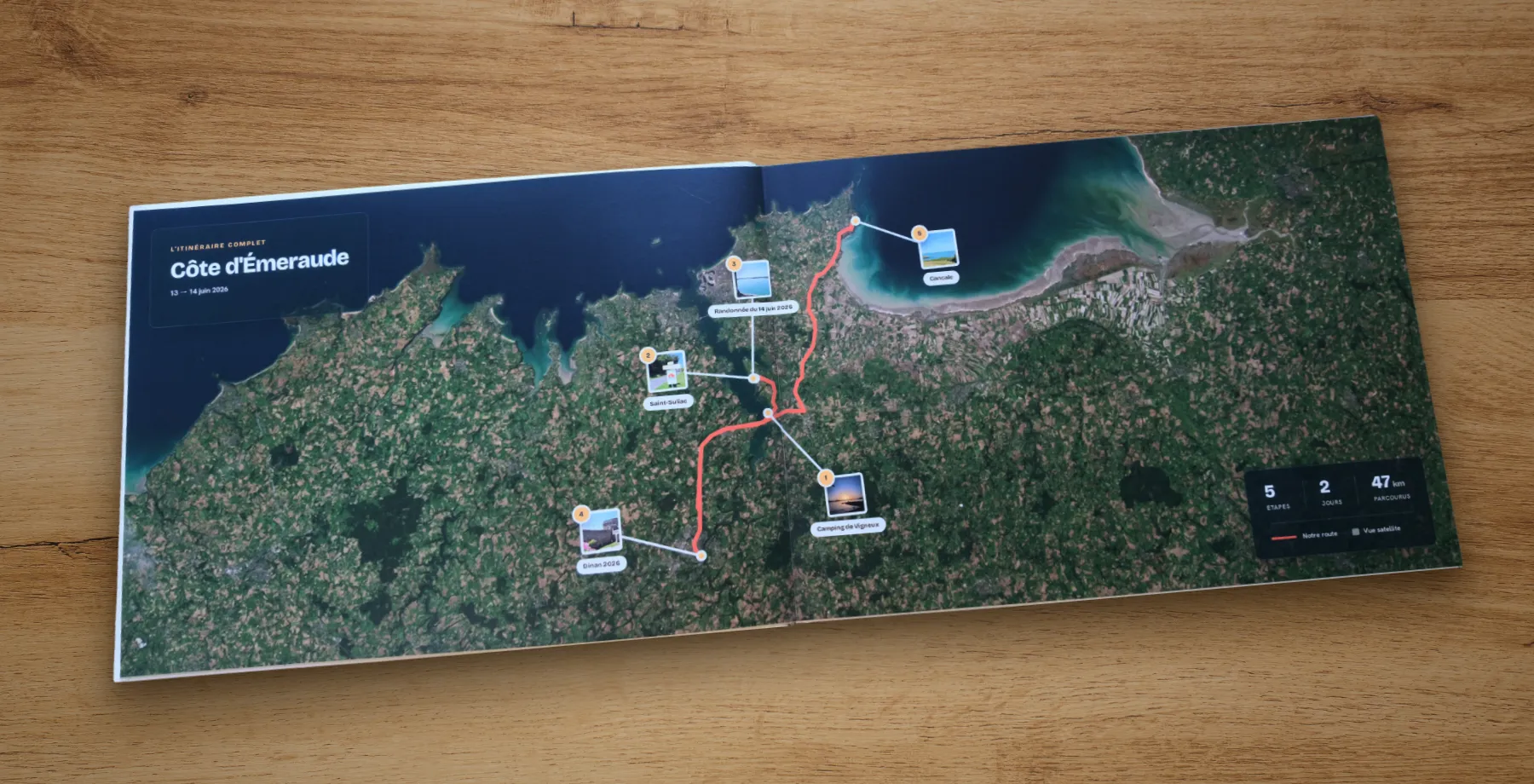 Le livre imprimé, ouvert sur une table en bois : la double page satellite de la Côte d'Émeraude, avec le tracé en corail, cinq étapes, deux jours et 47 km parcourus.